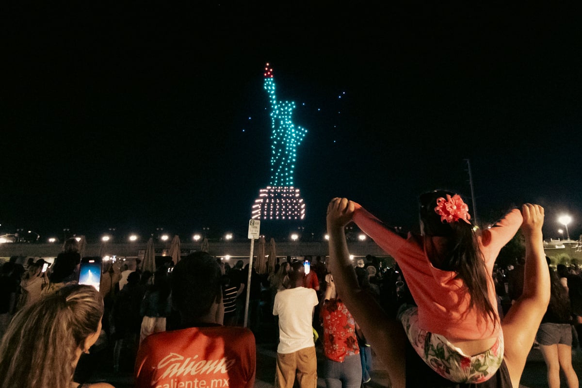 A glowing drone formation of the Statue of Liberty captivates a crowd at a nighttime event.