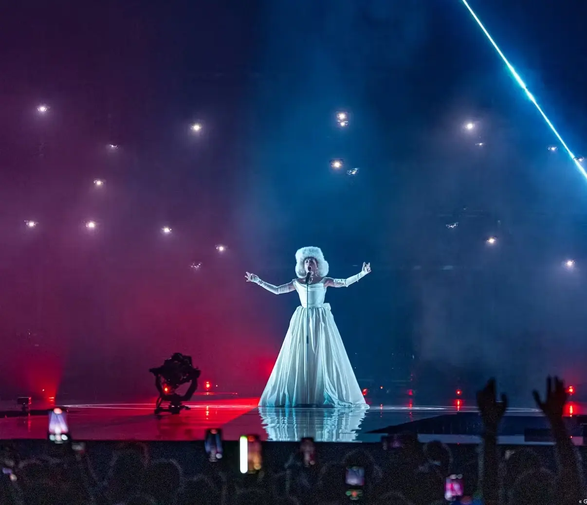 Performer on stage beneath drones lit red and blue during an indoor show