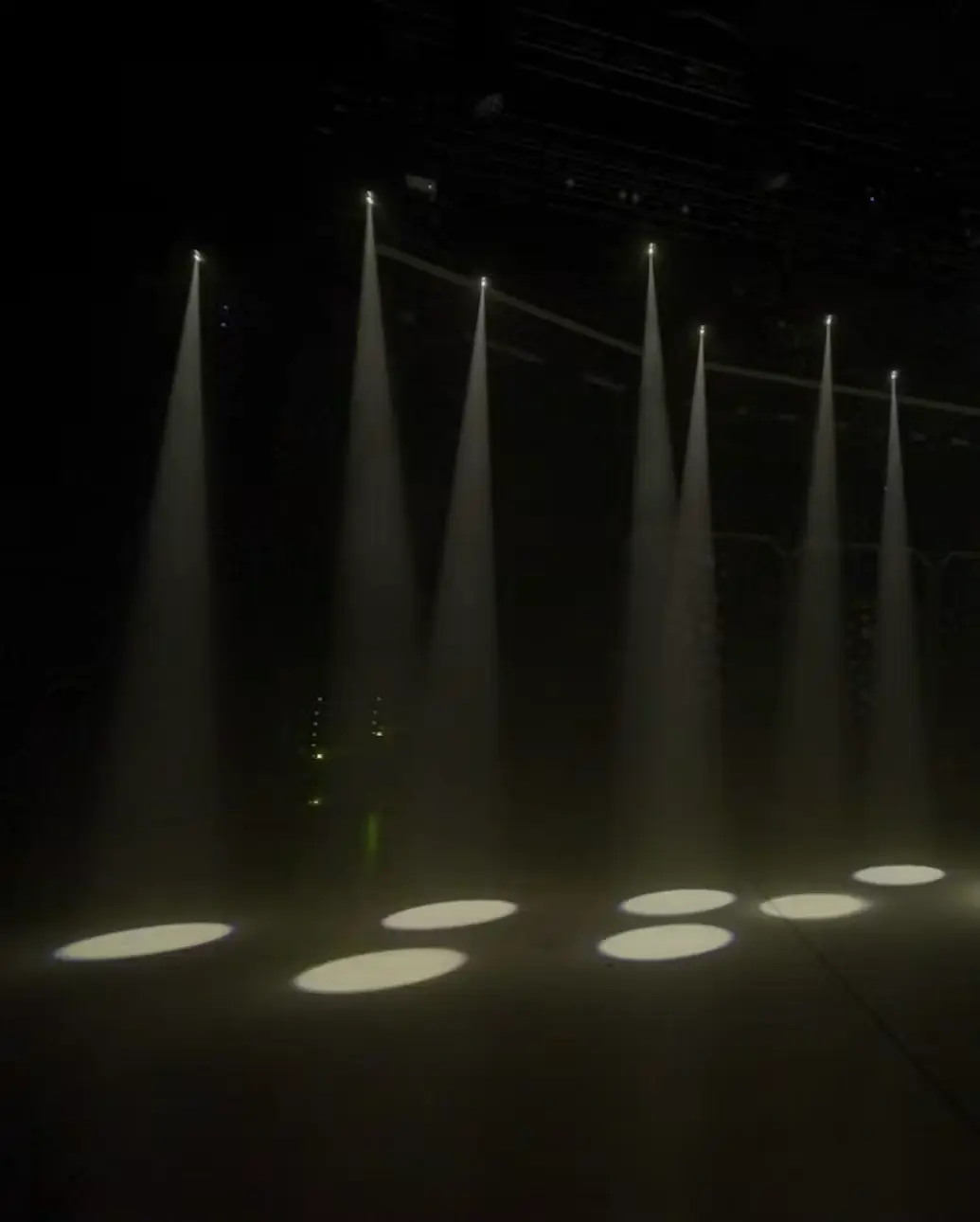 Mini searchlight beams from drones over a dark stage floor