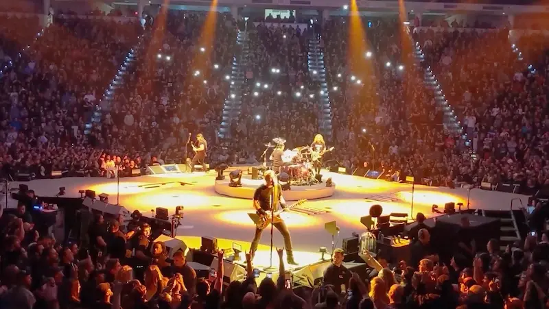 Band performing in the round to a packed arena with stage lighting