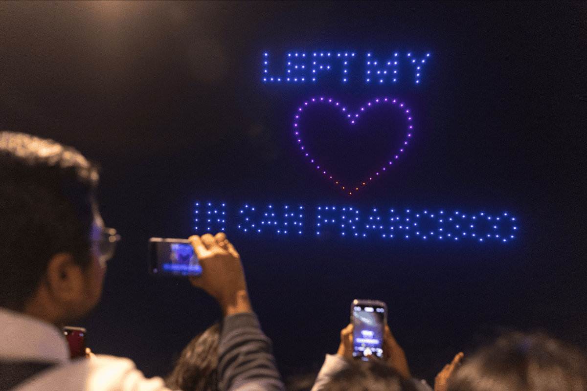 Spectators photograph drone light show displaying “Left My Heart in San Francisco” at night sky