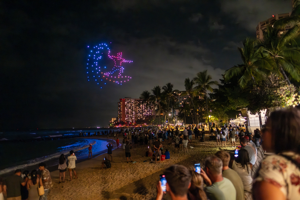 a drone show makes the image of a surfer while the audience watches from the beach